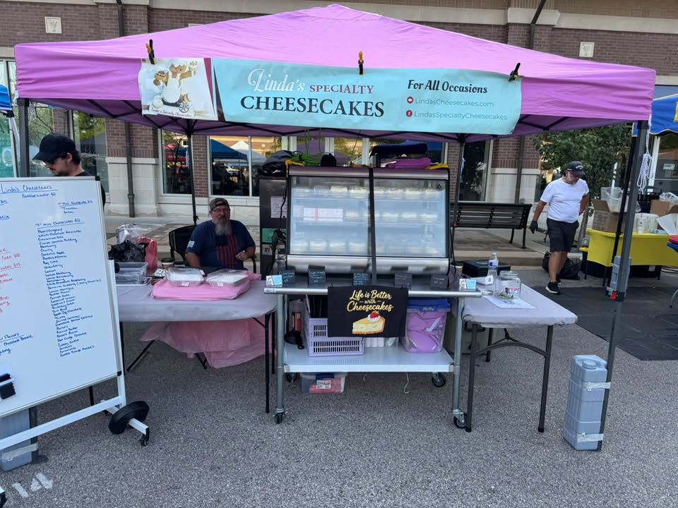Linda's Specialty Cheesecakes booth at a local market, with the display case full of cheesecakes.