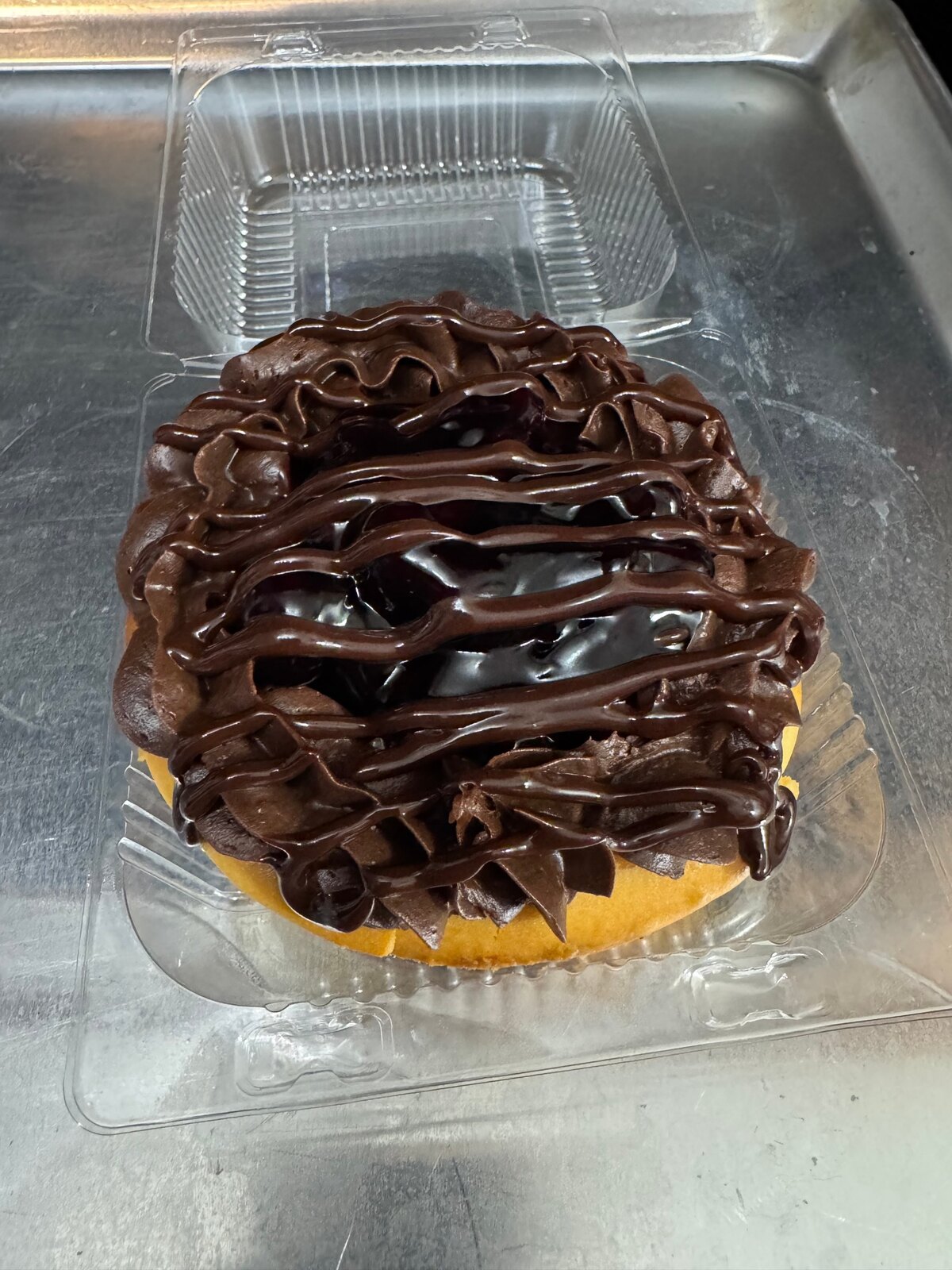 Chocolate blueberry cheesecake with chocolate frosting rosettes and a glossy chocolate drizzle in a clear container.