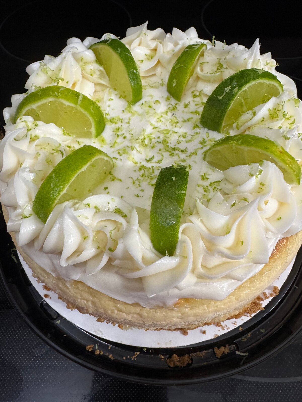 Key lime cheesecake topped with piped whipped cream, lime wedges, and lime zest.