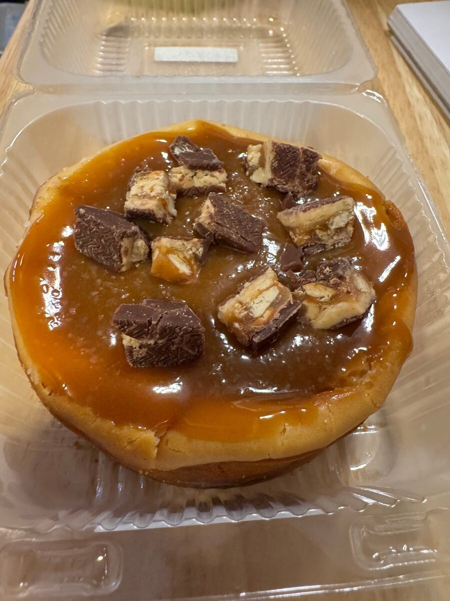 Salted caramel cheesecake topped with caramel and chopped Snickers pieces.